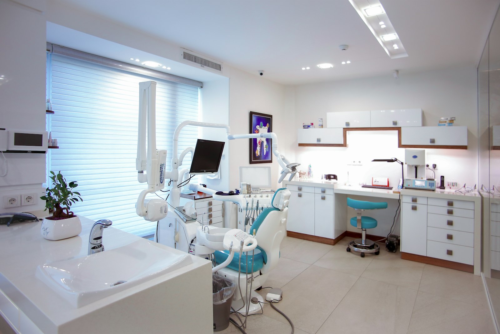 A bright, modern dental treatment room with a teal chair and white cabinetry